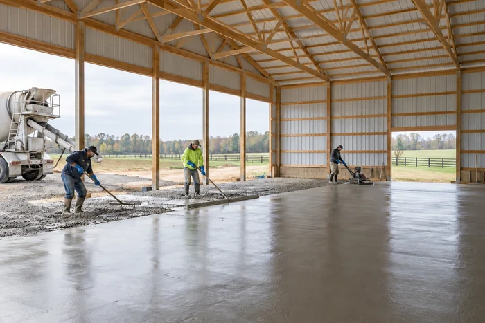 Crew placing and finishing a concrete floor inside a pole barn.